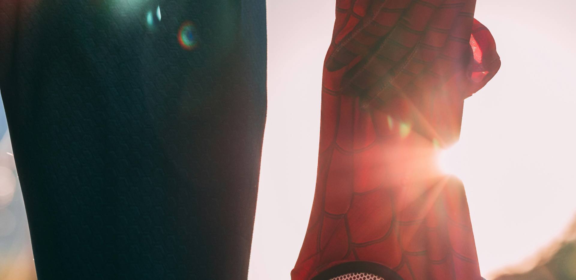 Das Bild zeigt eine Figur von hinten, die neben ihrem Oberschenkel eine Spiderman-Maske in der herabhängenden Hand hält. Das Bild zeigt eine Figur von hinten, die neben ihrem Oberschenkel eine Spiderman-Maske in der herabhängenden Hand hält.