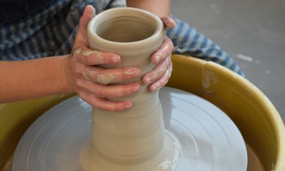 Man sieht eine Person die ein Stück Ton auf einer Drehscheibe mit Ihren Fingern formt. Man sieht eine Person die ein Stück Ton auf einer Drehscheibe mit Ihren Fingern formt.
