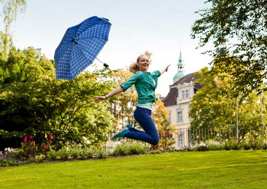 Ein junges Mädchen springt in die Luft und wirft den Regenschirm weg.