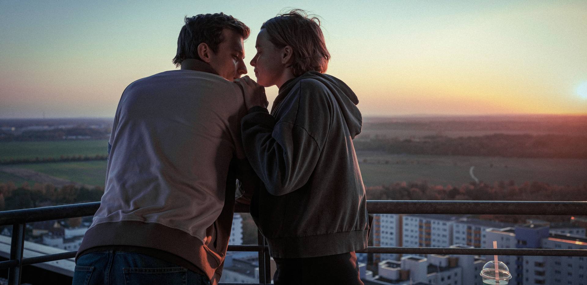 Auf dem Bild sind 2 Personen zu erkennen, die sich nahestehen. Links steht eine männlich gelesene Person und rechts steht eine weiblich gelesene Person. Im Hintergrund ist ein Sonnenauf- oder untergang zu erknnen. Auf dem Bild sind 2 Personen zu erkennen, die sich nahestehen. Links steht eine männlich gelesene Person und rechts steht eine weiblich gelesene Person. Im Hintergrund ist ein Sonnenauf- oder untergang zu erknnen.