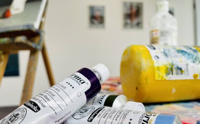 Auf dem Bild befinden sich mehrere Farbtuben und eine Staffelei Auf dem Bild befinden sich mehrere Farbtuben und eine Staffelei