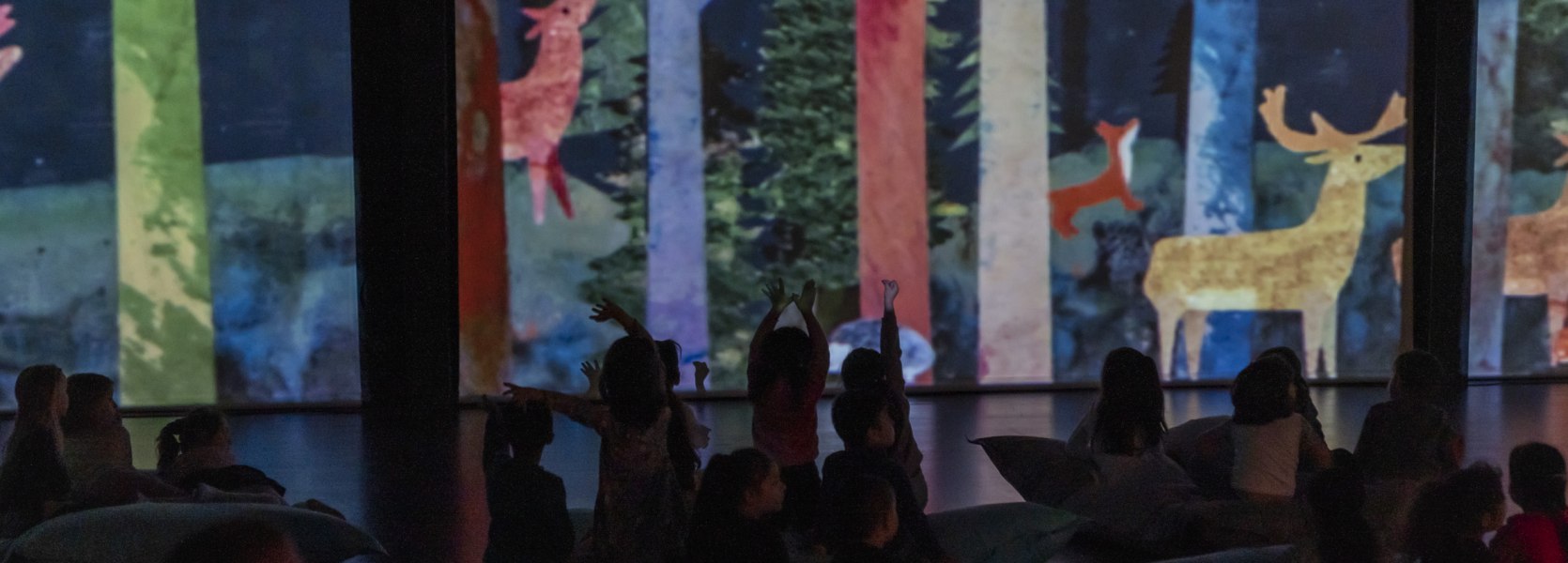 Im Vordergrund sind die Silhouetten von Kindern zu sehen, die die Projektionen im Hintergrund bejubeln.