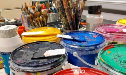 Auf dem Bild befinden sich verschiedene Farbeimer, Gläser mit Pinseln und weitere Malutensilien.