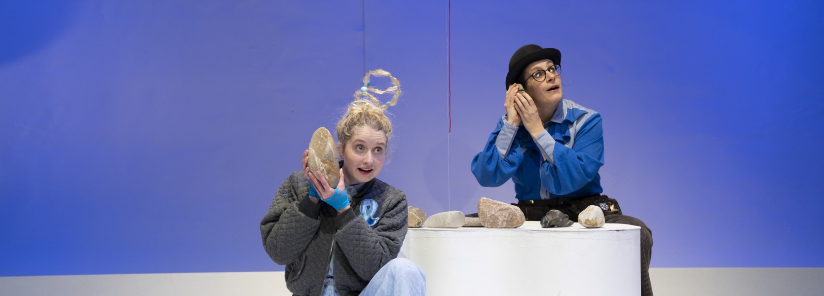Zwei Darstellerinnen halten sich Steine ans Ohr, zwischen ihnen schwebt ein Ballon.