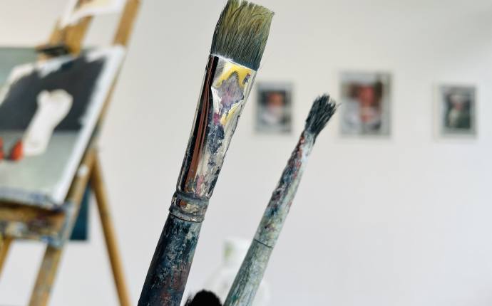 Auf dem Foto befinden sich einige Pinsel, im Hintergrund sieht man Gem&auml;lde.