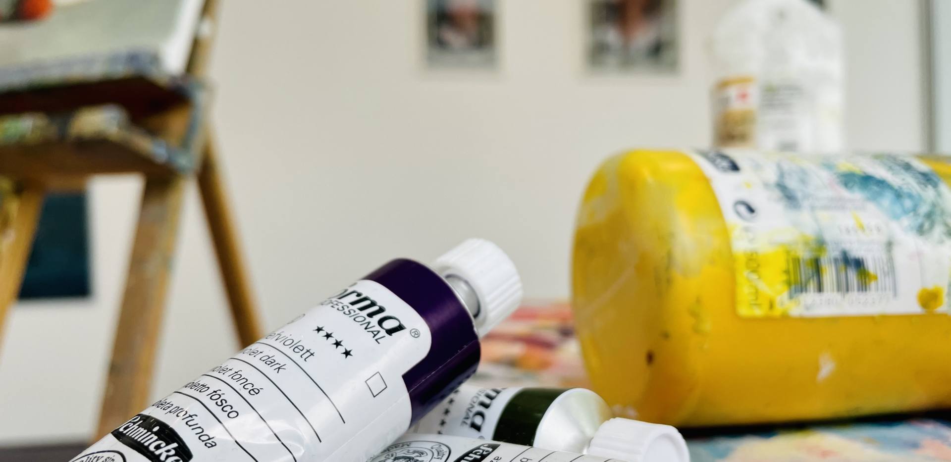 Auf dem Bild befinden sich mehrere Farbtuben und eine Staffelei Auf dem Bild befinden sich mehrere Farbtuben und eine Staffelei