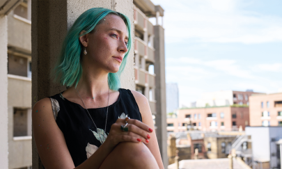 Junge Frau mit blauen Haaren sitzt an einem Fenster.