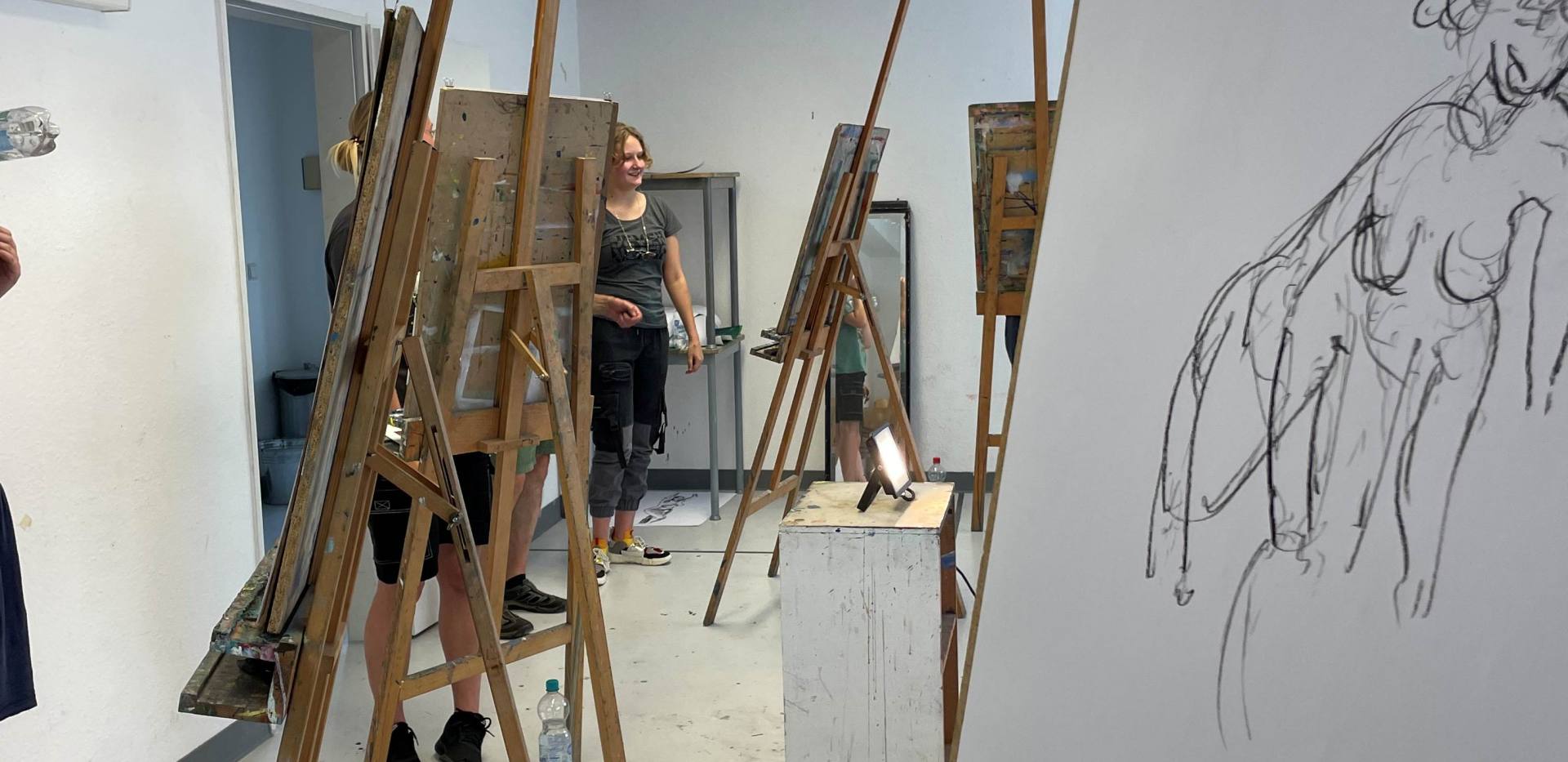 Auf dem Bild sieht man mehrere Staffeleien, im Vordergrund ist eine Aktzeichnung auf einer Staffelei. Auf dem Bild sieht man mehrere Staffeleien, im Vordergrund ist eine Aktzeichnung auf einer Staffelei.