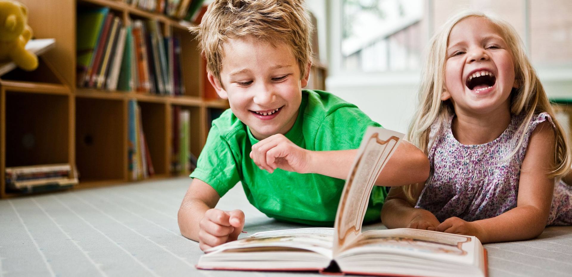 Zwei Kinder liegen auf dem Boden und lesen auf der Kinder- und Jugendbuchmesse ein Buch.