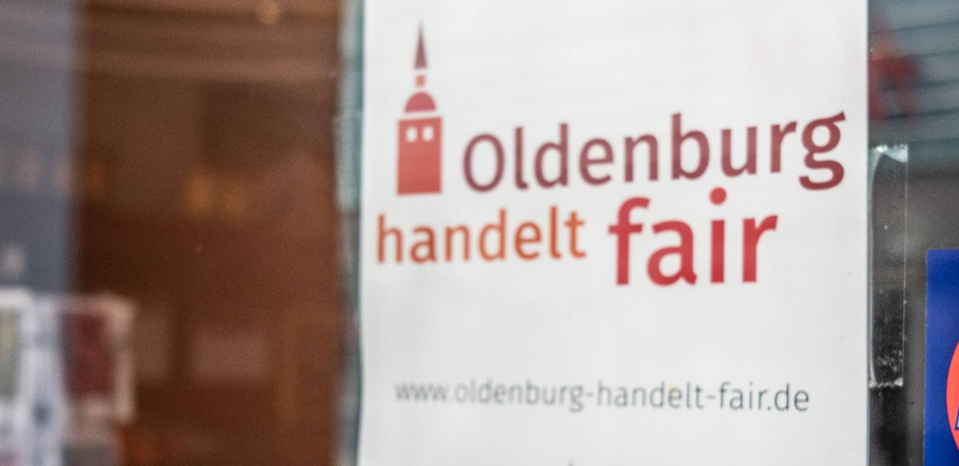Werbeschild "Oldenburg handelt fair" in einem Fenster.