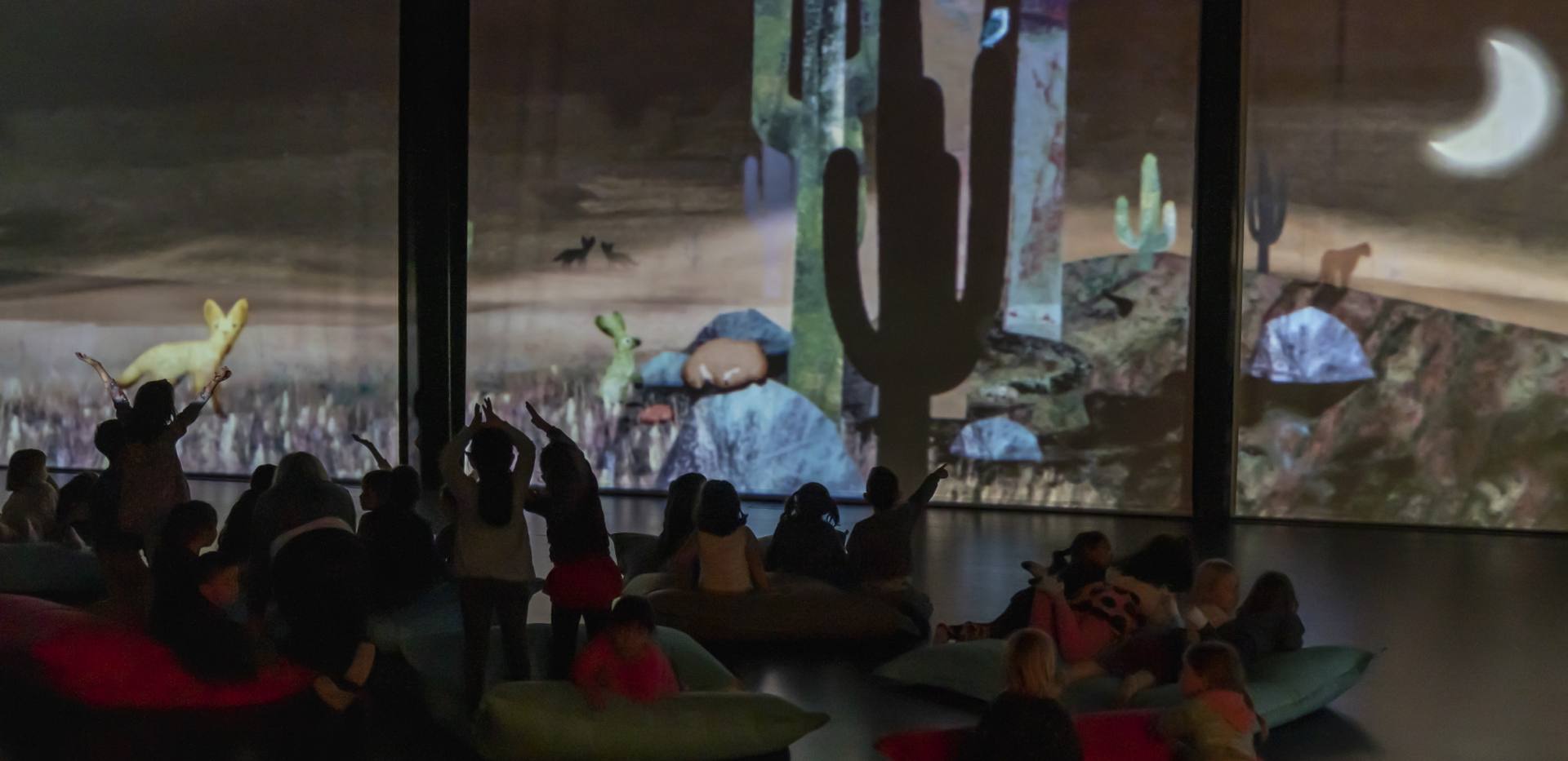 Im Vordergrund sind die Silhouetten von Kindern zu sehen, die die Projektionen im Hintergrund bejubeln. Im Vordergrund sind die Silhouetten von Kindern zu sehen, die die Projektionen im Hintergrund bejubeln.