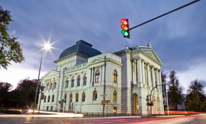 Das Oldenburgische Staatstheater von der gegenüberliegenden Straßenseite in der Abenddämmerung mit einer Ampel im Vordergrund.