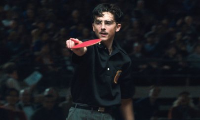 Im Bild ist eine männlich gelesene Person, die einen Tischtennisschläger mit der rechten Hand hält und gleichzeitig mit der gleichen Hand zu jemanden zeigt. Der Hintergrund ist dunkel und verschwommen. Im Bild ist eine männlich gelesene Person, die einen Tischtennisschläger mit der rechten Hand hält und gleichzeitig mit der gleichen Hand zu jemanden zeigt. Der Hintergrund ist dunkel und verschwommen.