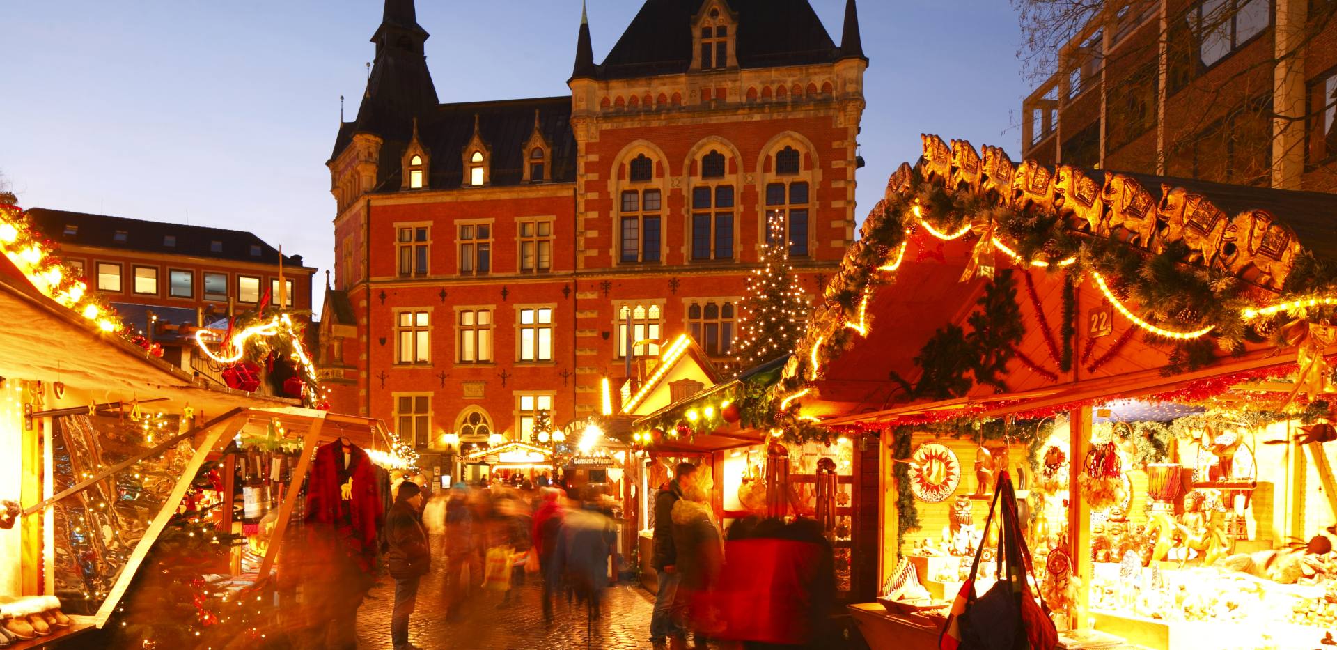 Beleuchtete Holzbuden auf dem Weihnachtsmarkt mit dem historischen Alten Rathaus im Hintergrund.