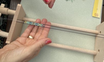 Auf dem Bild ist zu sehen, wie jemand Perlen webt.