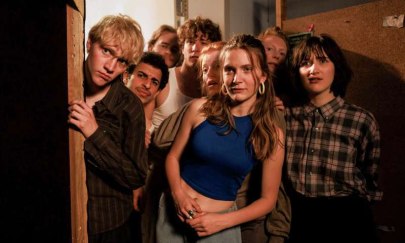 Eine Gruppe von 8 Menschen gucken um die Ecke in einen raum. Die Person ganz links guckt mit weitoffenen Augen. Die Person am weitestesten in der Mitte guckt mit einem eher negativen Blick. Die Person ganz rechts guckt verwundert.