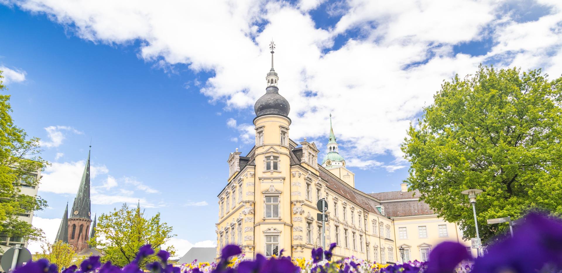 Oldenburger Schloss und St. Lamberti-Kirche mit Blumen im Vordergrund.