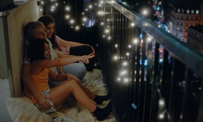 3 Personen sitzen auf einem Balkon in einer Stadt bei Nacht. Am Zaun des Balkon ist eine Lichterkette. Die Stadt im Hintergrund leuchtet. 3 Personen sitzen auf einem Balkon in einer Stadt bei Nacht. Am Zaun des Balkon ist eine Lichterkette. Die Stadt im Hintergrund leuchtet.