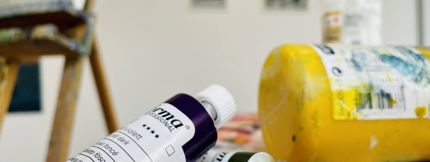 Auf dem Foto kann man verschiedene Farbtuben, Leinw&auml;nde und eine Staffelei erkennen.