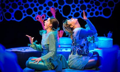 Zwei Performerinnen einander abgewandt auf einer B&uuml;hne in Unterwasseratmosph&auml;re