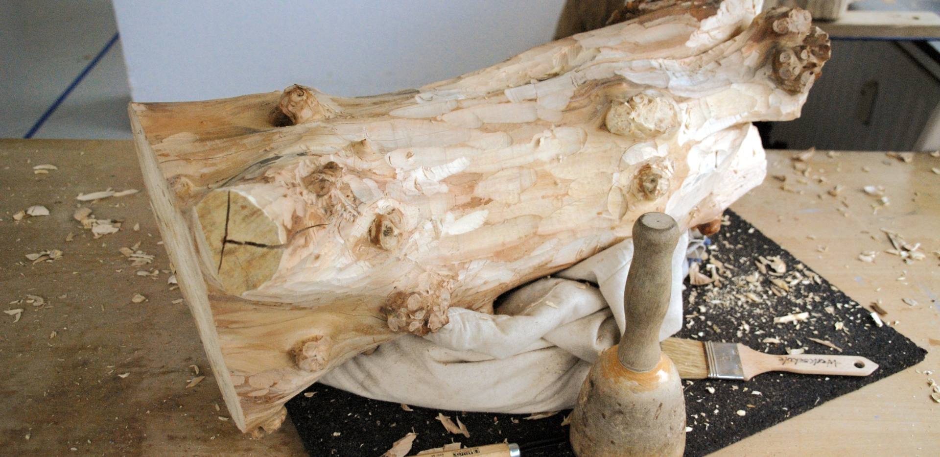 Man sieht ein Stück Holz welches gerade mit Hilfe von Werkzeugen bearbeitet wird.