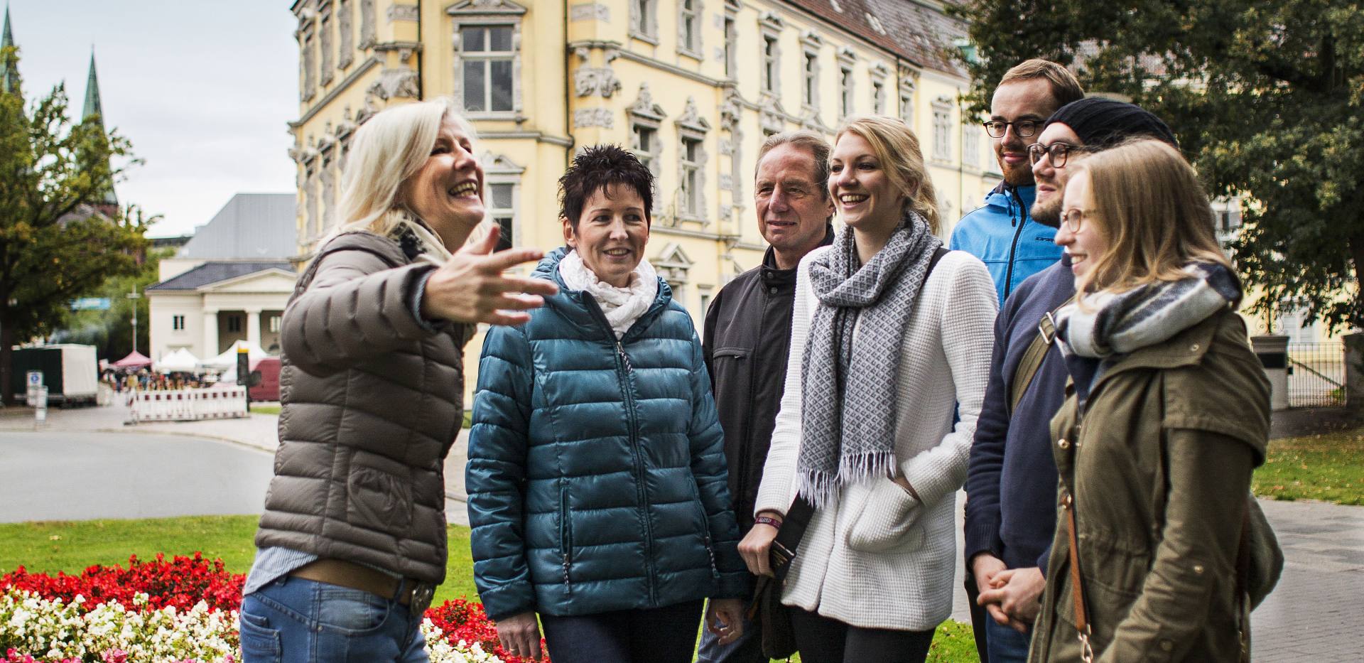 Eine kleine Gruppe mit einer Gästeführerin vor dem Oldenburger Schloss.