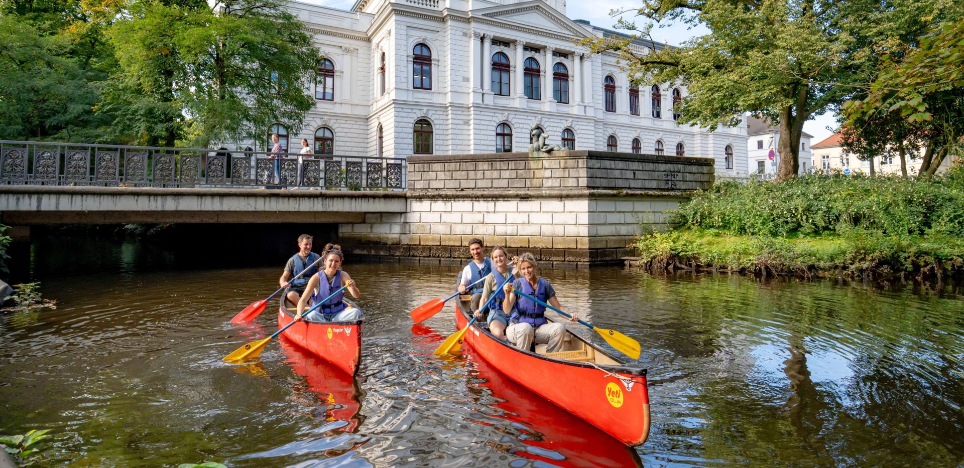 Zwei Kanus mit Teilnehmenden der Stadtführung „City Paddeln“. Sie fahren auf der Hausbäke vor dem Oldenburgischen Staatstheater. Zwei Kanus mit Teilnehmenden der Stadtführung „City Paddeln“. Sie fahren auf der Hausbäke vor dem Oldenburgischen Staatstheater.
