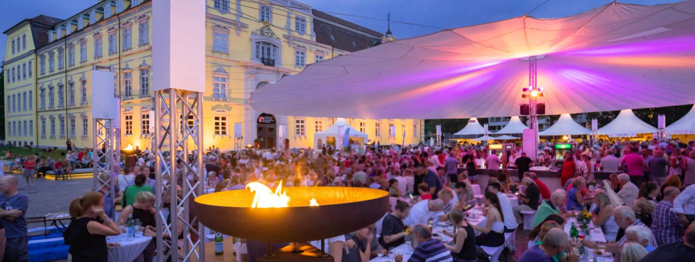 Vor dem Oldenburger Schloss sitzen viele Besucher bei der Veranstaltung Kochen am Schloss unter einem großen Sonnentuch.