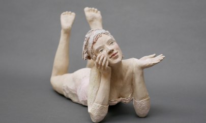 Man sieht eine kleine Figur aus Holz die auf dem Bauch liegt.