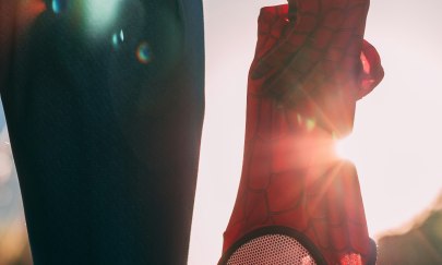 Das Bild zeigt eine Figur von hinten, die neben ihrem Oberschenkel eine Spiderman-Maske in der herabhängenden Hand hält. Das Bild zeigt eine Figur von hinten, die neben ihrem Oberschenkel eine Spiderman-Maske in der herabhängenden Hand hält.