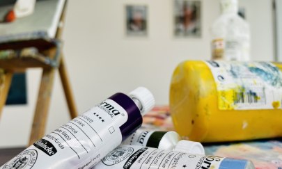 Auf dem Bild befinden sich mehrere Farbtuben und eine Staffelei Auf dem Bild befinden sich mehrere Farbtuben und eine Staffelei