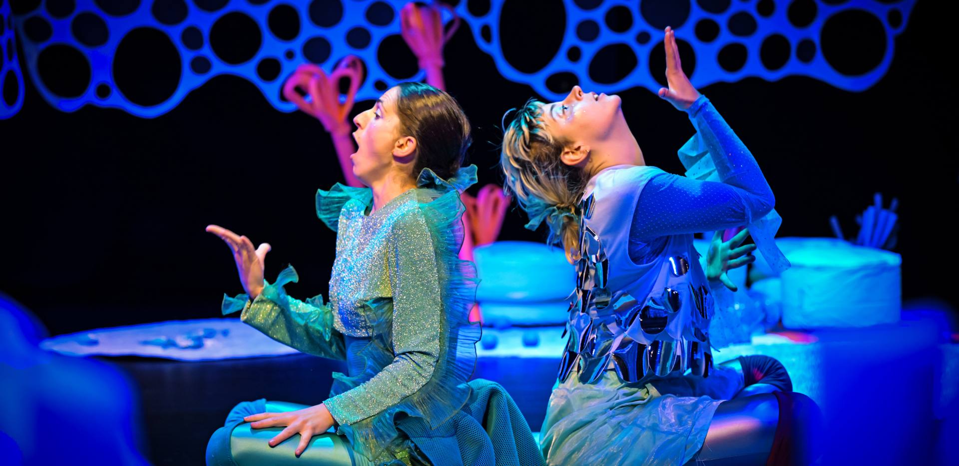 Zwei Performerinnen einander abgewandt auf einer B&uuml;hne in Unterwasseratmosph&auml;re