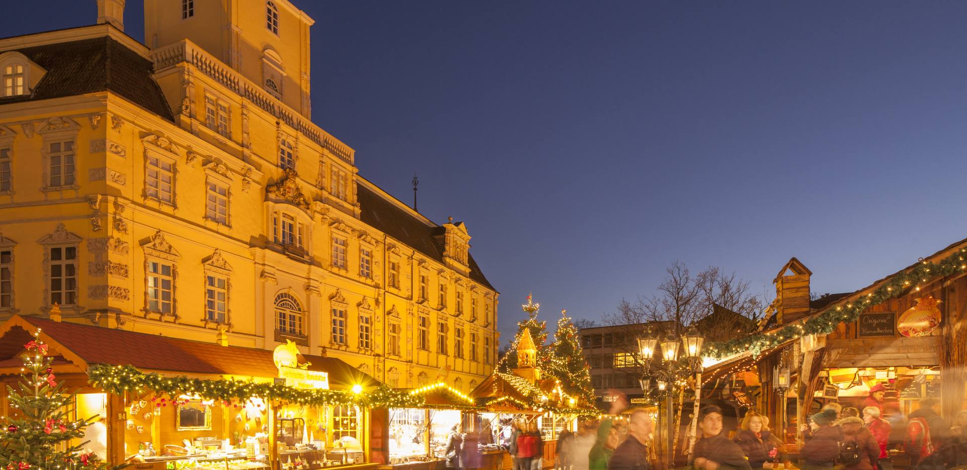 Beleuchtete Buden auf dem Weihnachtsmarkt mit Schloss.