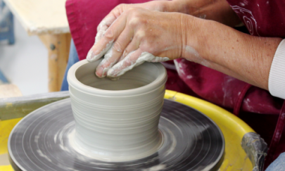 Eine Person arbeitet an einem Gefäß auf der Drehscheibe.