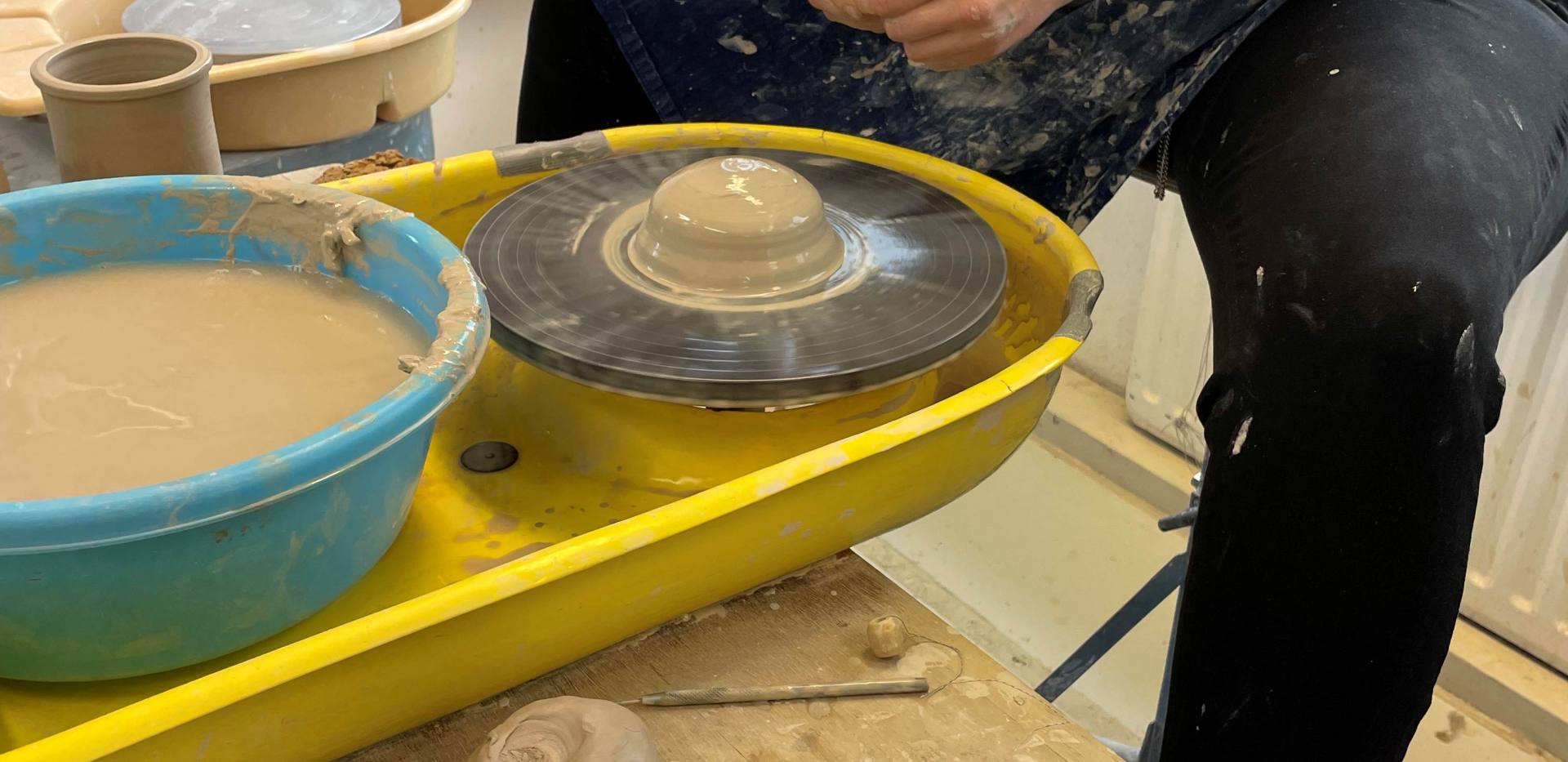 Auf dem Bild sieht man eine Person die an der Drehscheibe ein Stück Ton bearbeitet. Auf dem Bild sieht man eine Person die an der Drehscheibe ein Stück Ton bearbeitet.