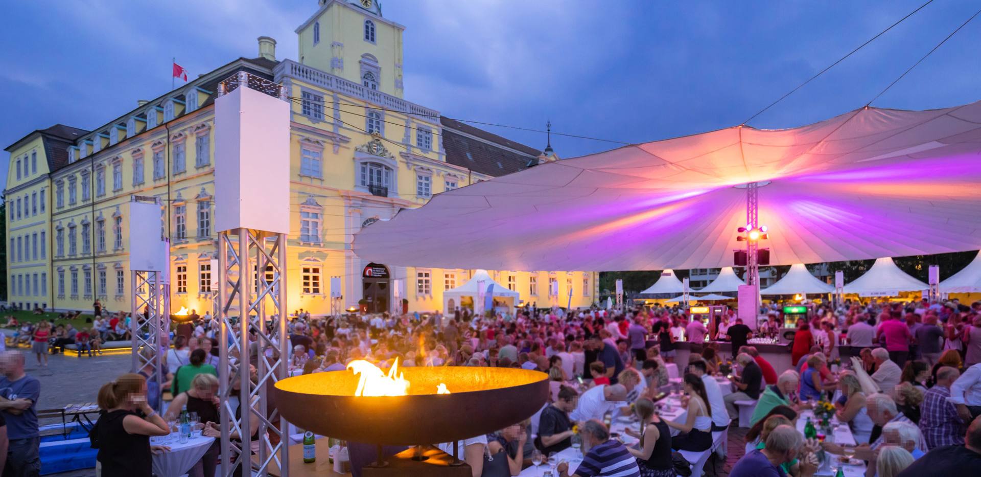 Vor dem Oldenburger Schloss sitzen viele Besucher bei der Veranstaltung Kochen am Schloss unter einem großen Sonnentuch.