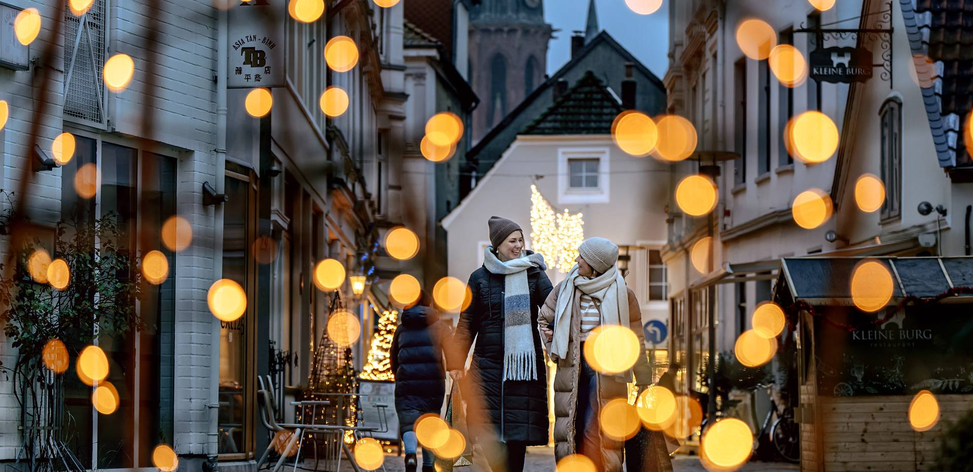 Zwei Frauen gehen durch die weihnachtlich beleuchtete Burgstraße in Oldenburg. 