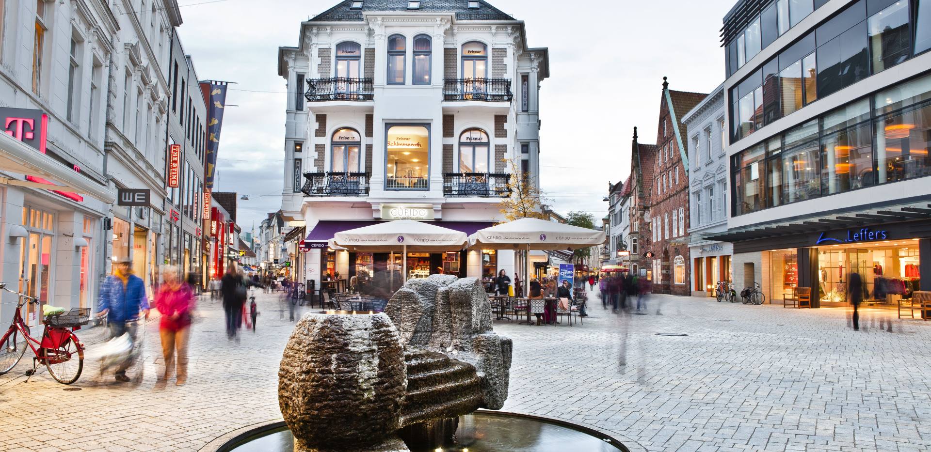 Fußgängerzone mit Brunnen im Vordergrund.