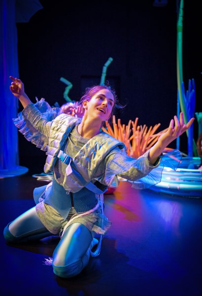 Eine Performerin gestikulierend auf einer B&uuml;hne in Unterwasseratmosph&auml;re