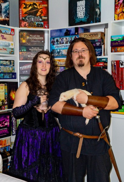 Die Inhabenden Erika und Martin haben nicht nur, wie es der Name "Zum flinken Frettchen" vermuten lässt, eigene Frettchen, sondern sind auch noch große Fantasy-Nerds. Rollenspiele, Brettspiele, Computerspiele,... alles, was einen in andere Welten eintauchen lässt, begeistert sie seit vielen Jahren.Hier seht ihr die beiden in mittelalterlicher Gewandung mit ihren flauschigen Mitbewohnern und umgeben von einem Teil ihrer umfangreichen Spielesammlung.