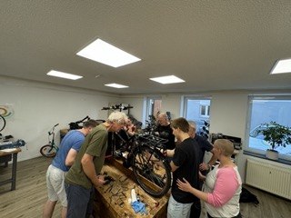 In einer Werkstatt stehen mehrere Menschen um ein Fahrrad herum und ein Dozent erklärte Reparatur In einer Werkstatt stehen mehrere Menschen um ein Fahrrad herum und ein Dozent erklärte Reparatur