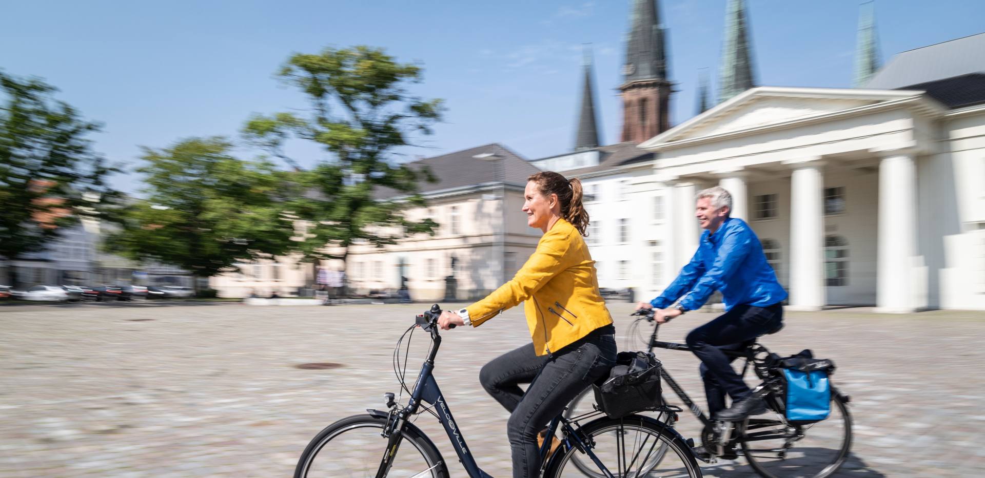 Eine Frau und ein Mann fahren mit ihrem Fahrrad über den Oldenburger Schlossplatz. 