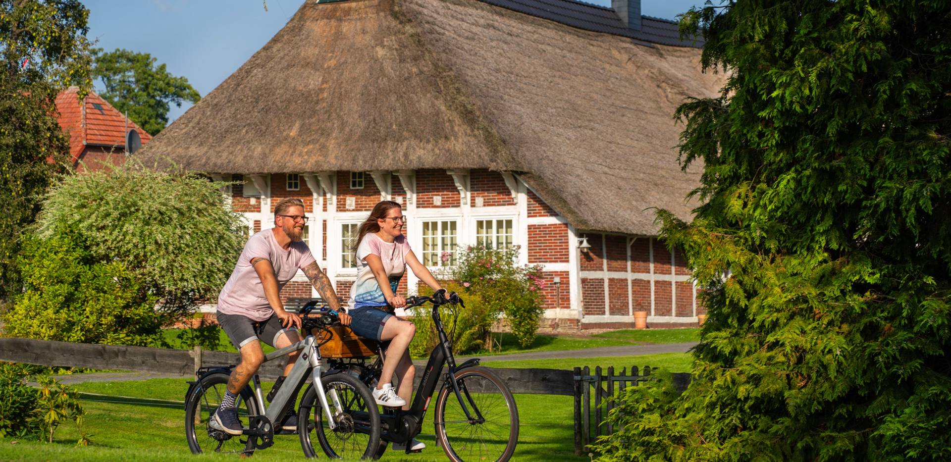 Radfahrer auf der Route um Oldenburg vor einem Reetdachhaus in Wesermarsch