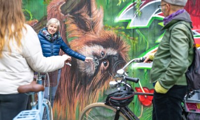 Eine Gästeführerin zeigt zwei Touristen Street Art mit einem Affen in Oldenburg bei einer geführten Radtour