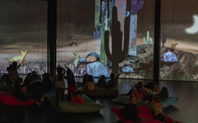 Im Vordergrund sind die Silhouetten von Kindern zu sehen, die die Projektionen im Hintergrund bejubeln. Im Vordergrund sind die Silhouetten von Kindern zu sehen, die die Projektionen im Hintergrund bejubeln.