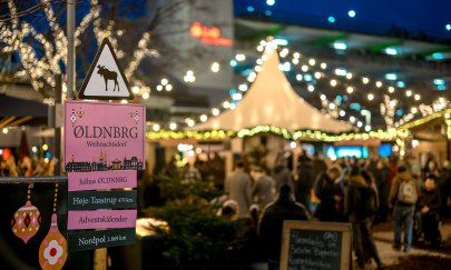 Skandinavisches Weihnachtsdorf Oldenburg Schild Skandinavisches Weihnachtsdorf Oldenburg mit beleuchtetem Markt im Hintergrund