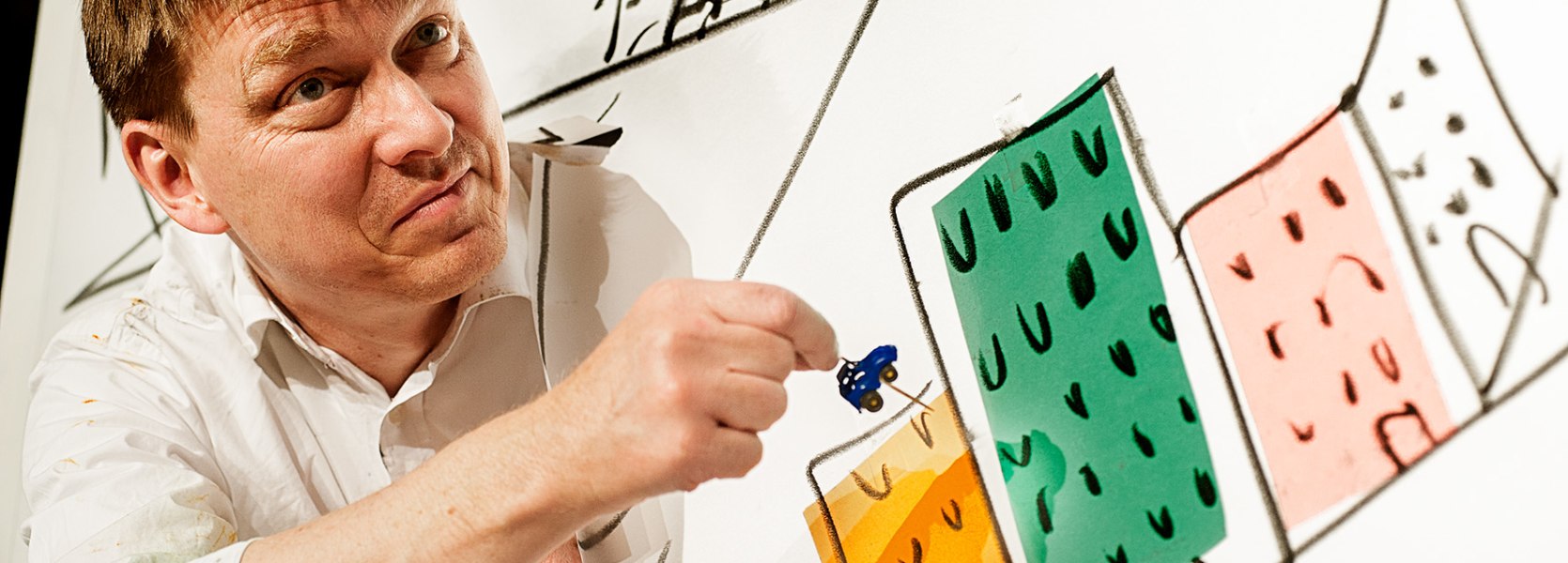 Spieler ragt aus einer mit H&auml;usern bemalten Wand mit seinem Oberk&ouml;rper heraus und m&ouml;chte eine Nadel in die Wand stecken.