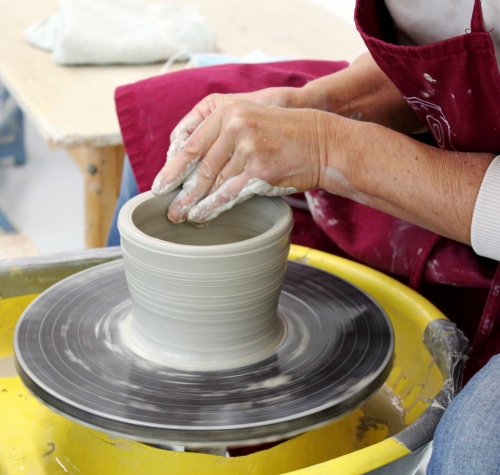 Eine Person arbeitet an einem Gefäß auf der Drehscheibe.