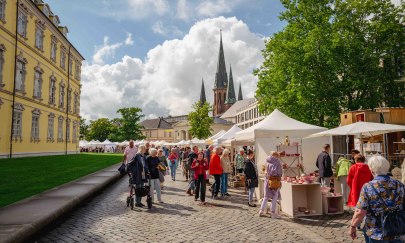 Links sieht man das gelbe Oldenburger Schloss und im fernen Hintergrund die Lambertikirche. Im Vordergrund sieht man verschiedene Menschen an den Keramikmarktst&auml;nden bummeln.