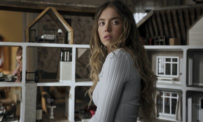 Im Bild ist eine weiblich gelesene Person zu erkennen, die mit verwundertem Gesichtsausdruck über ihre Schulter nach hinten guckt. Die Person steht drinnen. Im Hintergrund ist ein Modell eines Hauses zu erkennen. Im Bild ist eine weiblich gelesene Person zu erkennen, die mit verwundertem Gesichtsausdruck über ihre Schulter nach hinten guckt. Die Person steht drinnen. Im Hintergrund ist ein Modell eines Hauses zu erkennen.